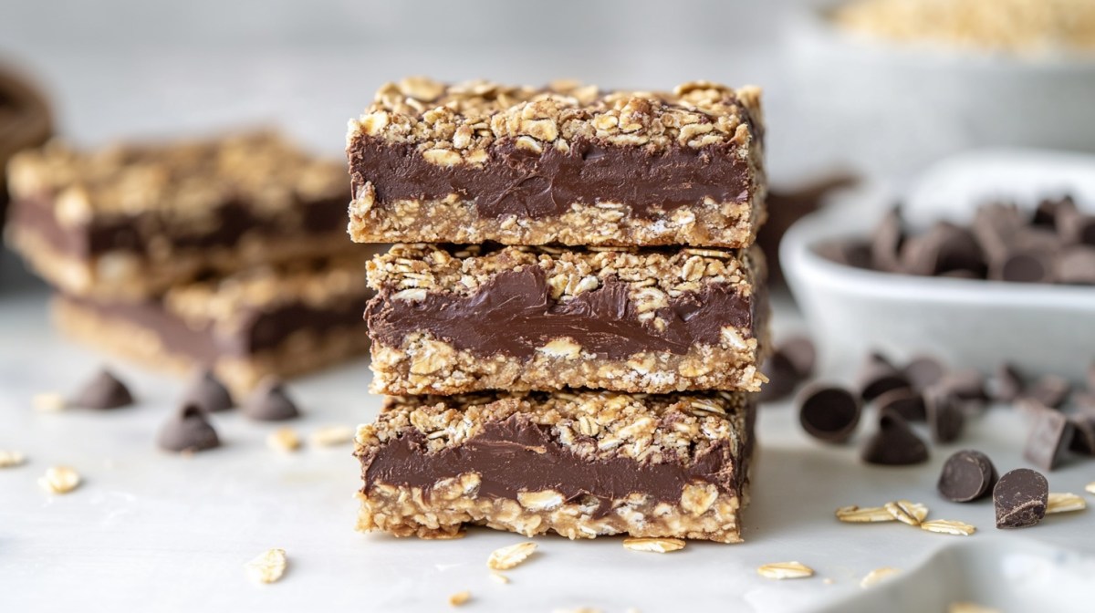 3 chocolate oatmeal bars stacked on top of each other, some ingredients like chocolate and oatmeal blurred out in the background.