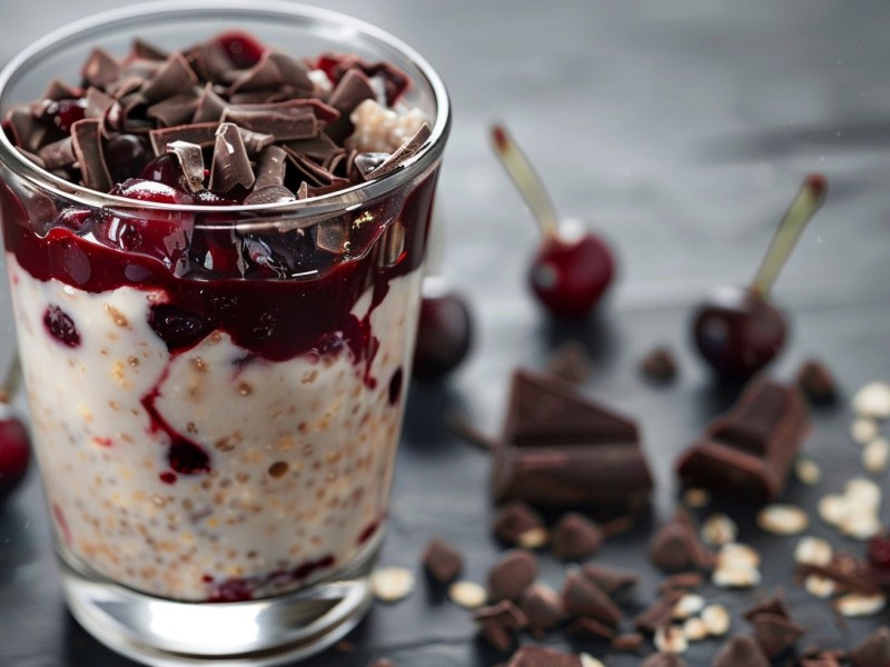 A clear jar filled with oats chocolates and cherries sits on a gray table.