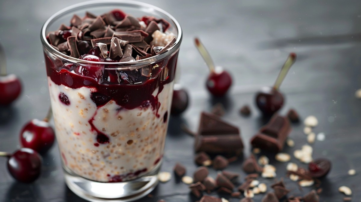 A clear jar filled with oats chocolates and cherries sits on a gray table.