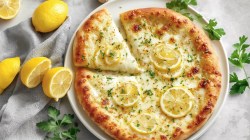 A lemon pizza in overhead view. Next to it are fresh ingredients.