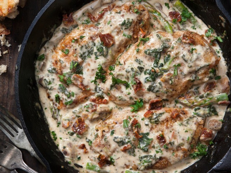 Chicken in parmesan sauce in a pan, photographed from above. Beside it are cutlery and breadcrumbs.