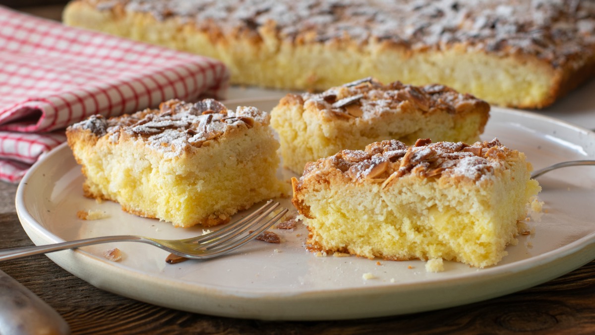 3 pieces of sheet cake butterkuchen on a plate, with the rest of the cake on a baking sheet and a kitchen towel in the background.