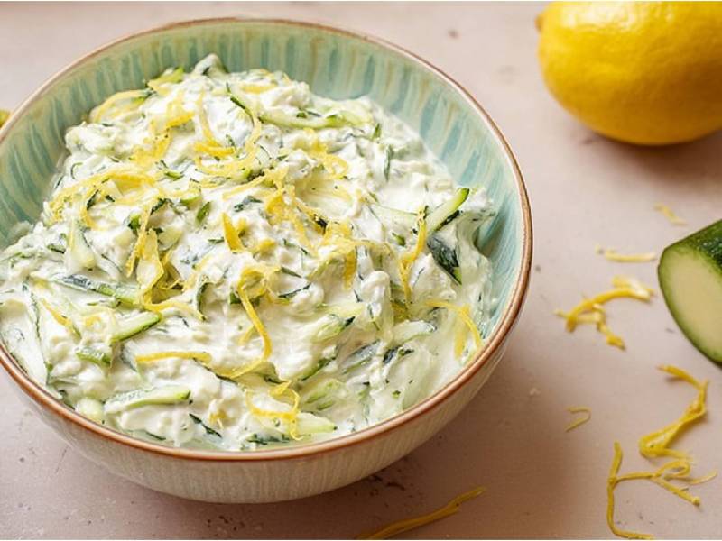 Bowl of zucchini tzatziki, zucchini and lemon next to it